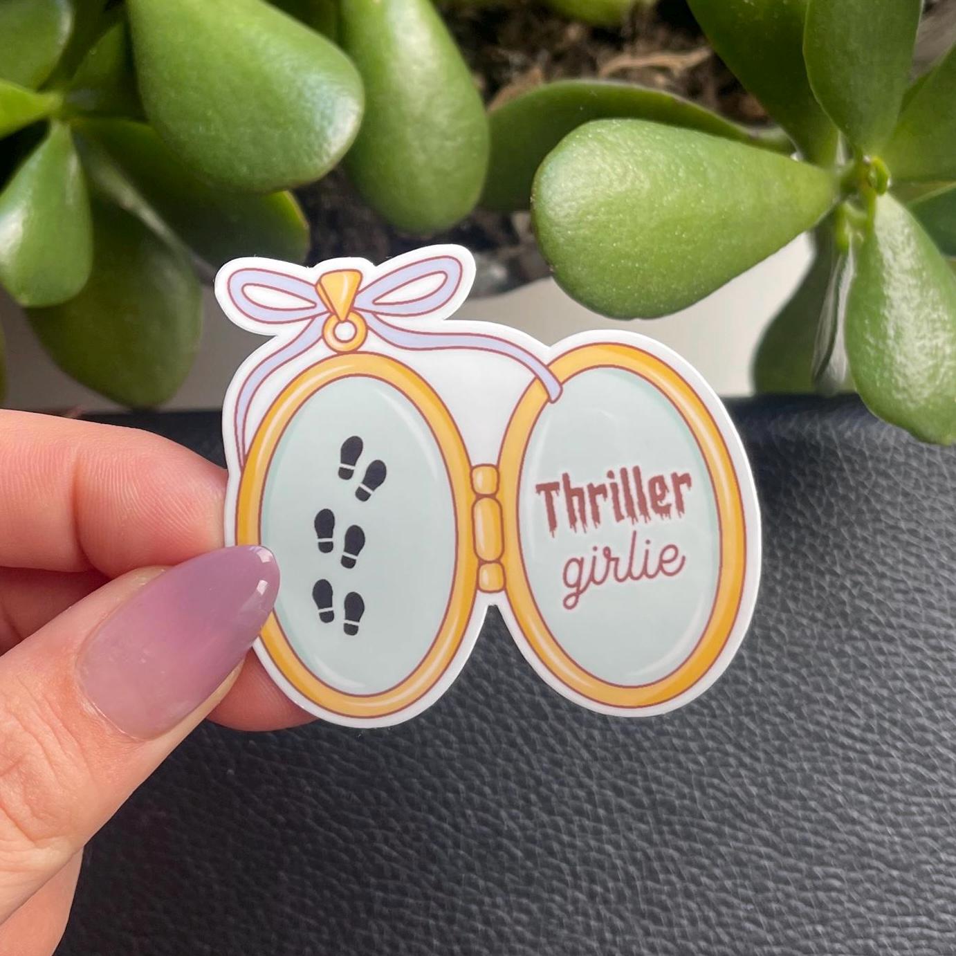 Sticker with 'Thriller girlie' design held by a hand against a plant background