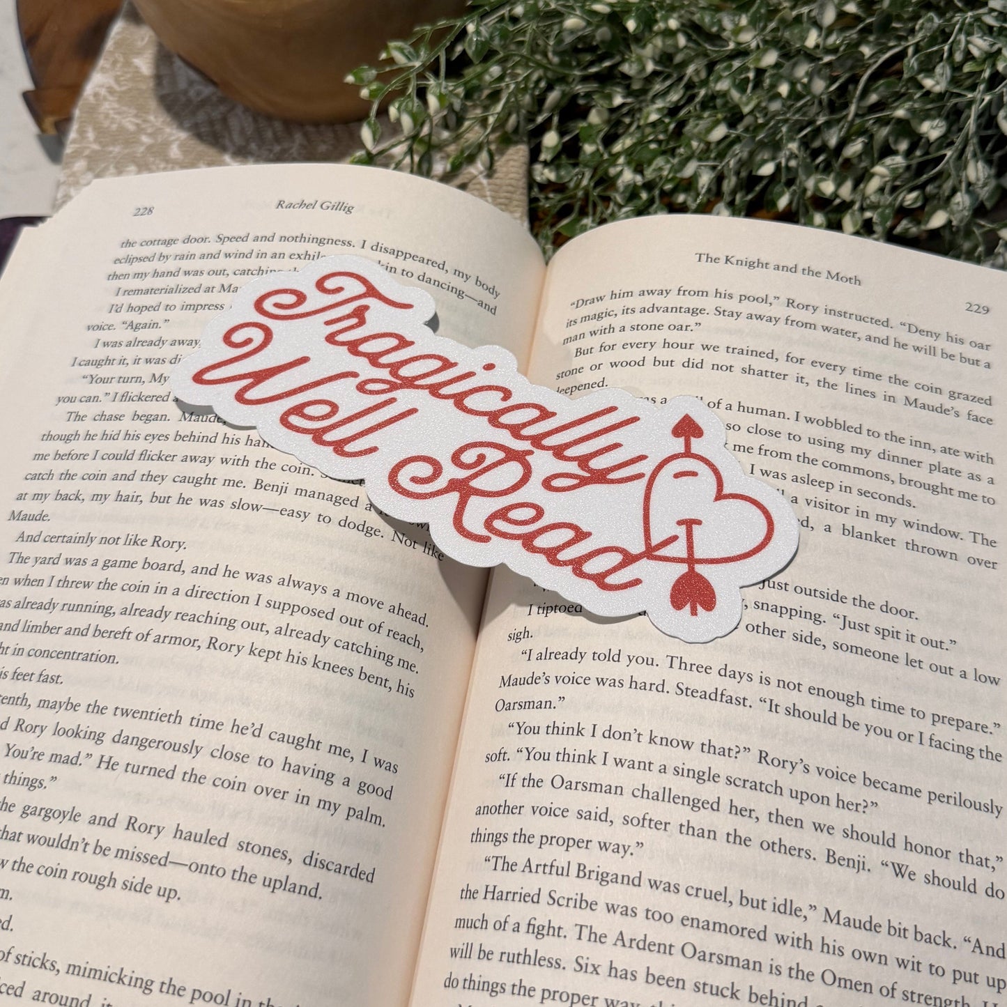 Open book with a decorative bookmark on a surface with a candle and plant.