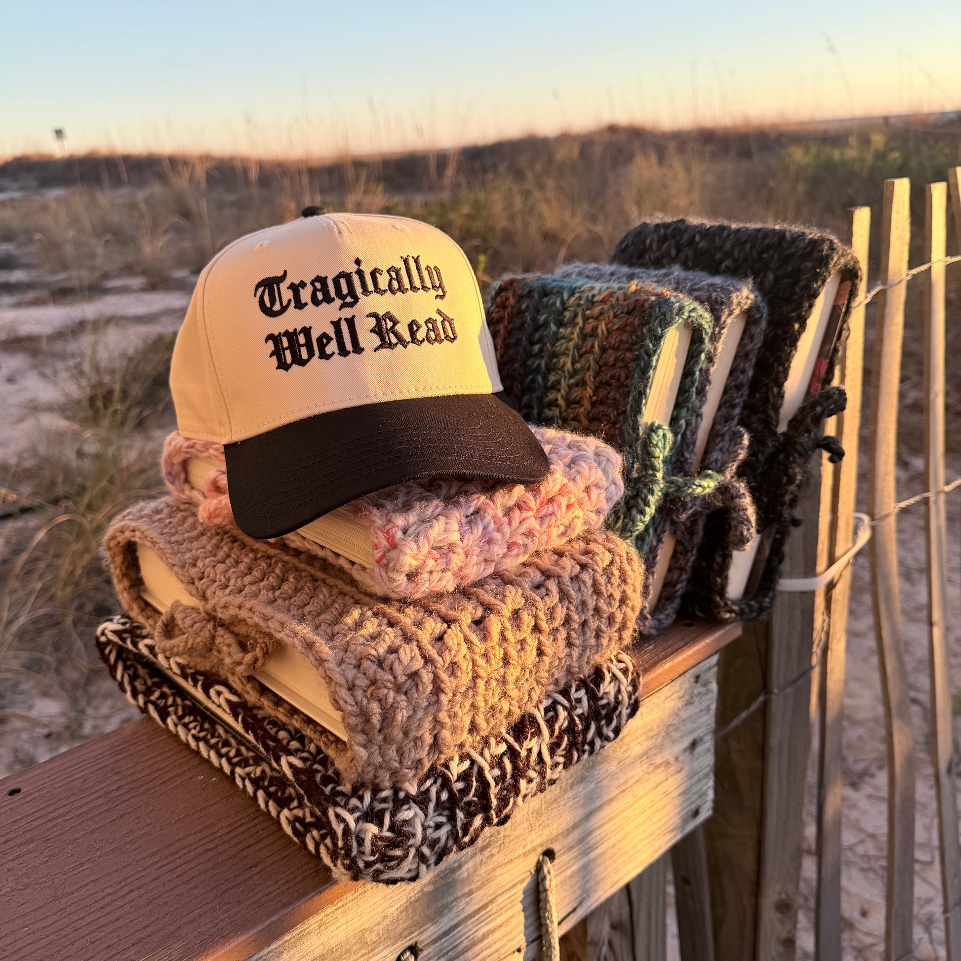 Collection of crochet book covers on a wooden surface with a 'Tragically Well Read' cap.