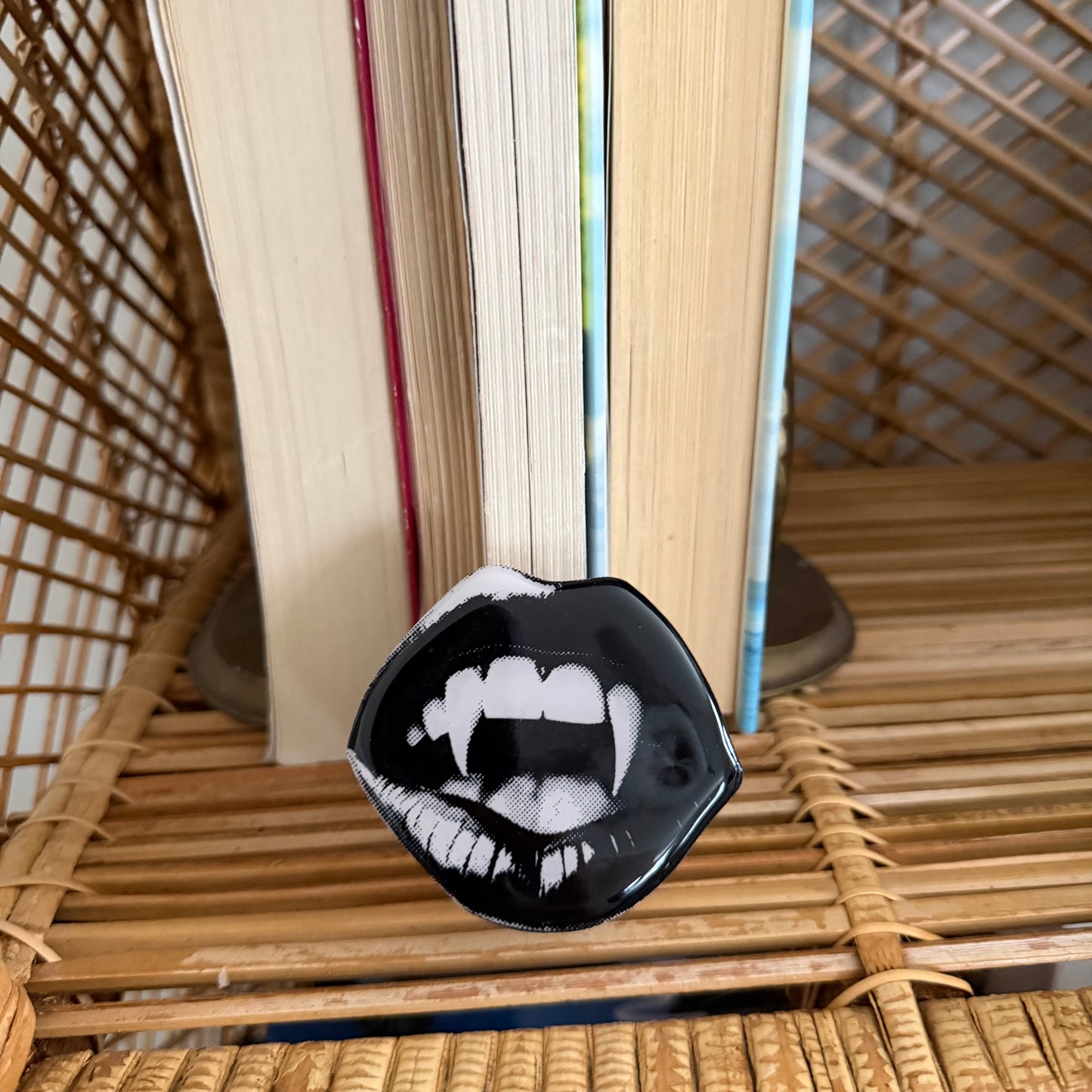 Black and white vampire mouth phone grip on a wicker surface with books in the background