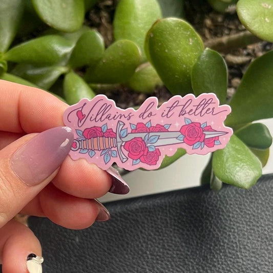 Hand holding a pink sticker with text and roses against a green plant background