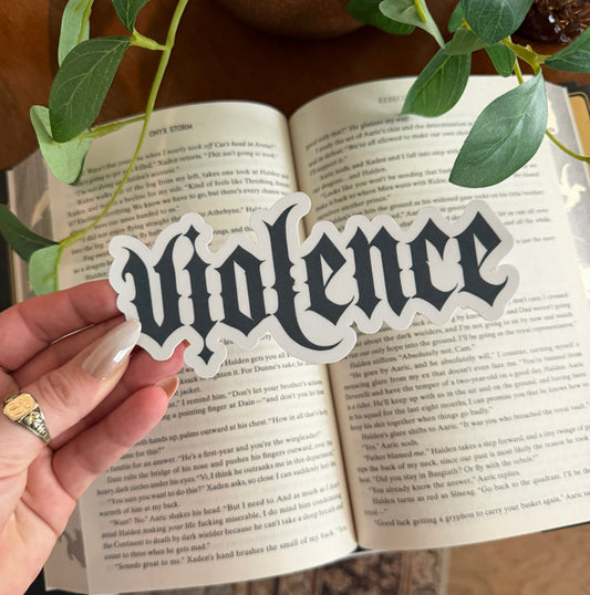 Hand holding a decorative bookmark with text over an open book, surrounded by plants.