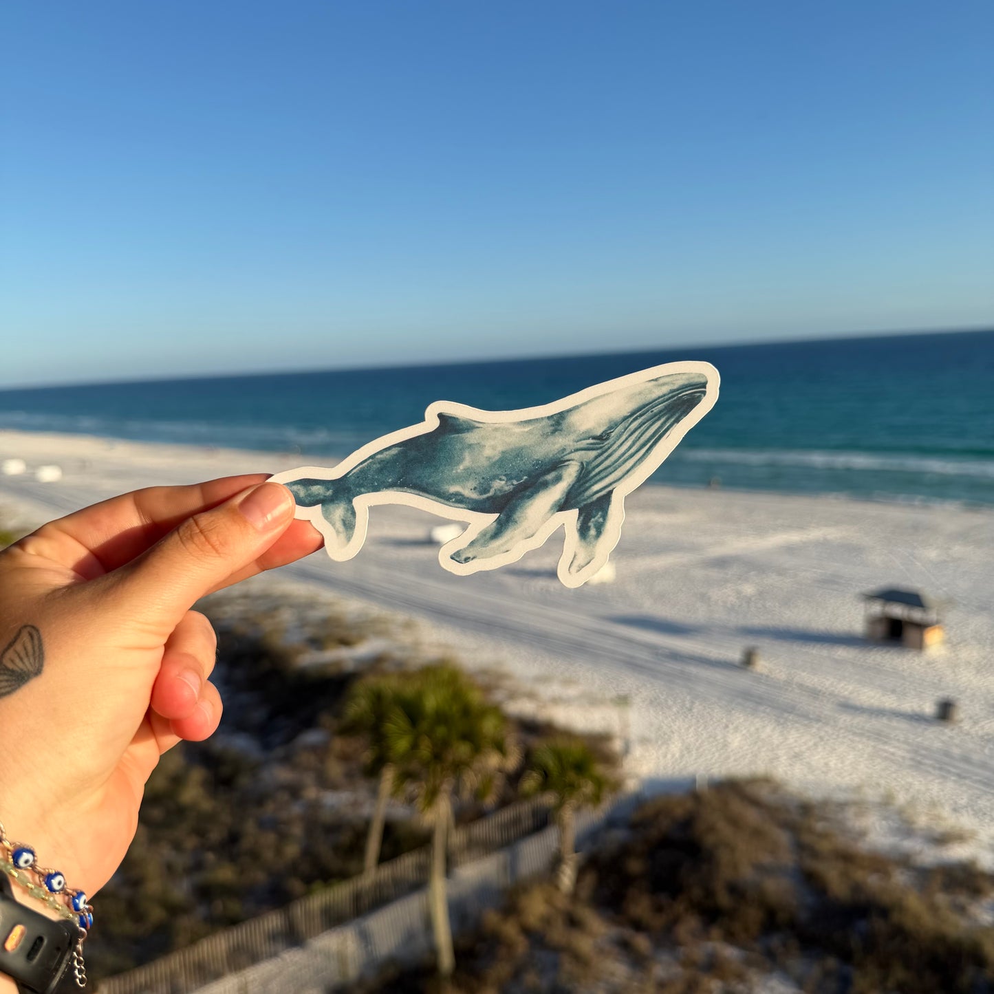 Hand holding a whale-shaped bookmark with a beach in the background