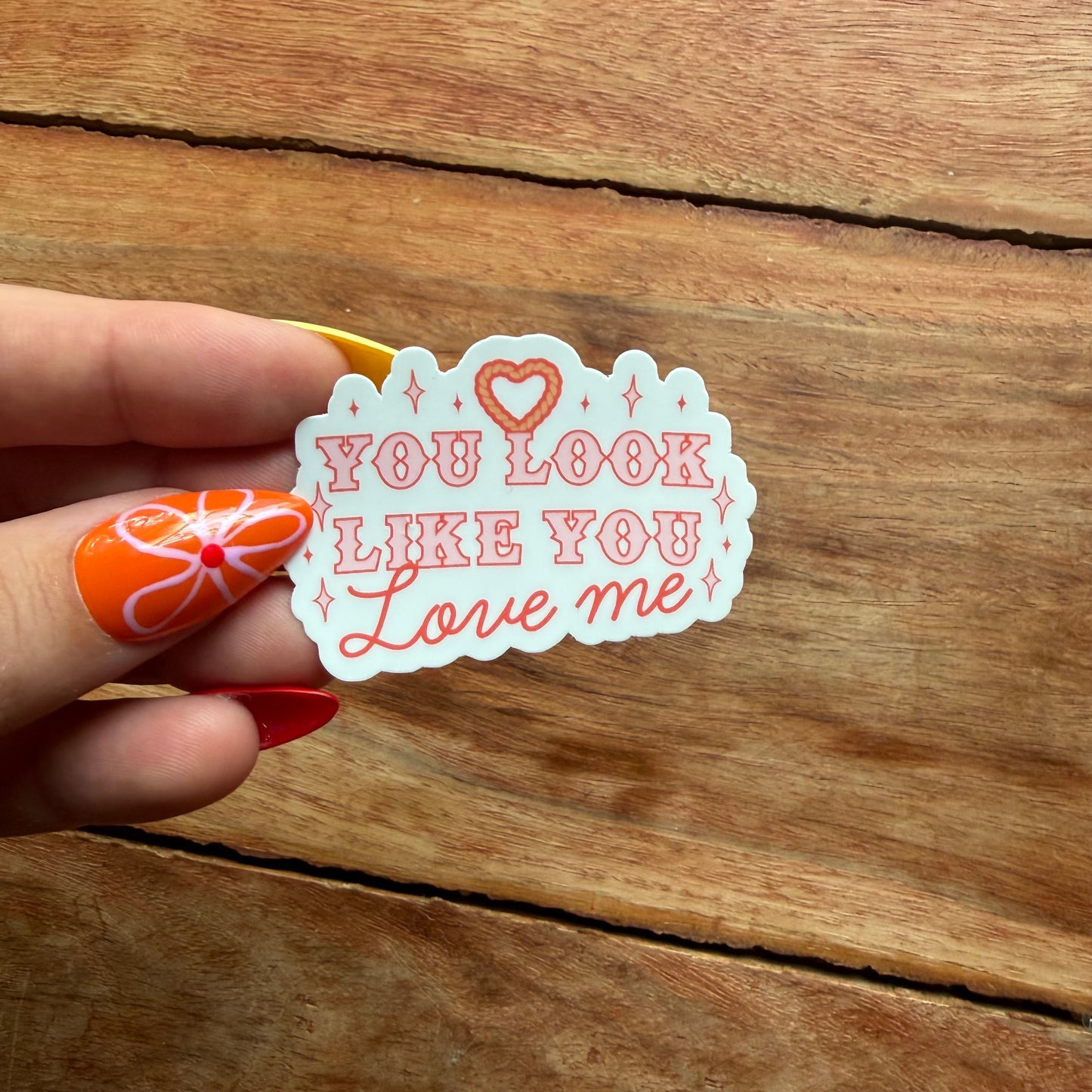 a hand  holding a white sticker that says you look like you love me over a wooden surface